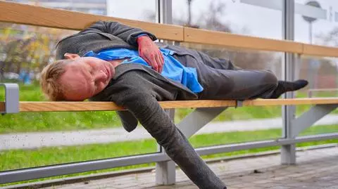 Kadr z serialu Na Wspólnej. Doktor Hoffer (Kazimierz Mazur) leży pijany na przystanku autobusowym.